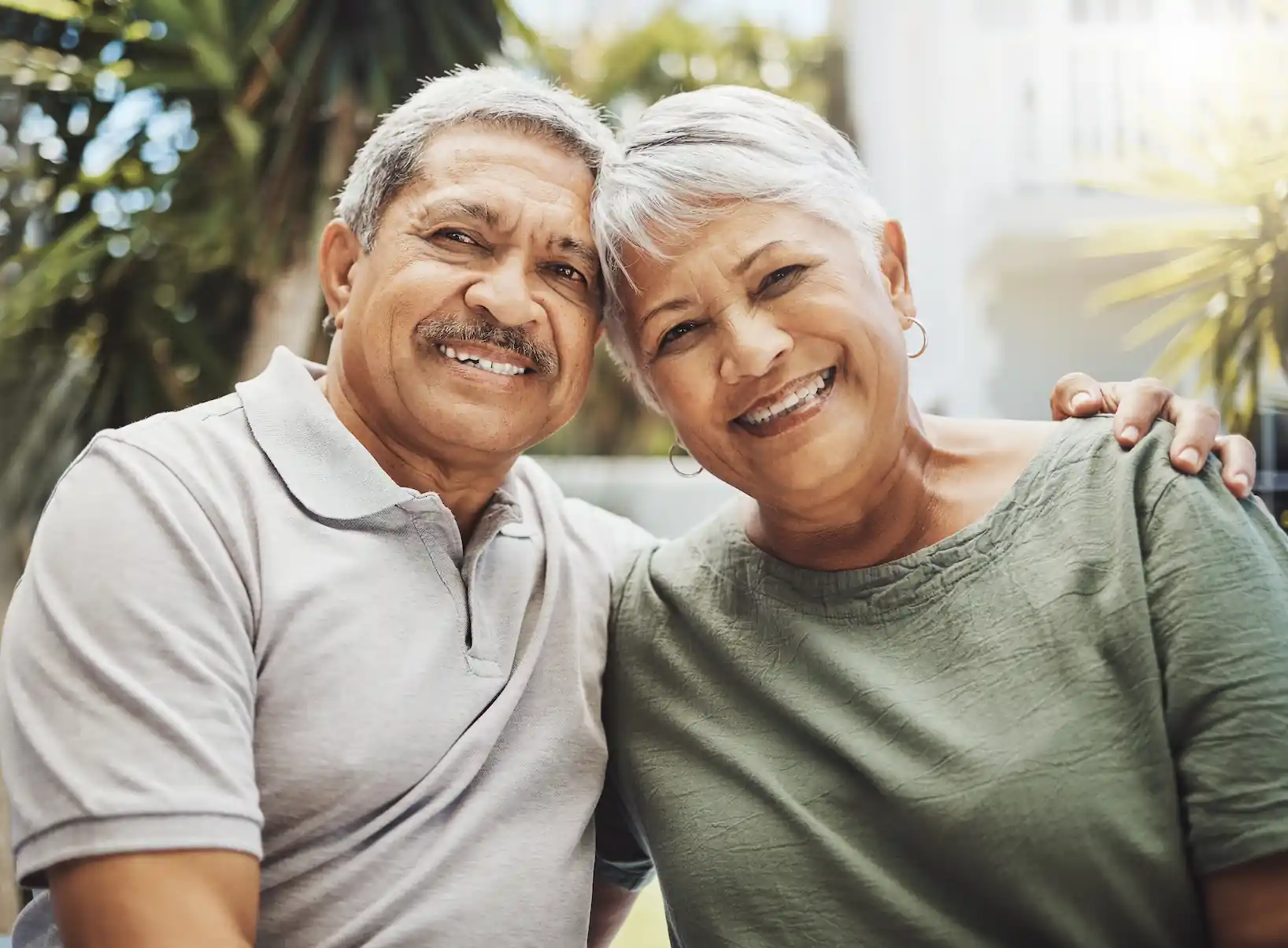 Una pareja de adultos mayores sonriendo, sentados juntos al aire libre